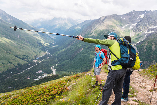 A group of hikers with backpacks and tracking sticks rest and stands in the mountains listening to their guide - Фото, изображение