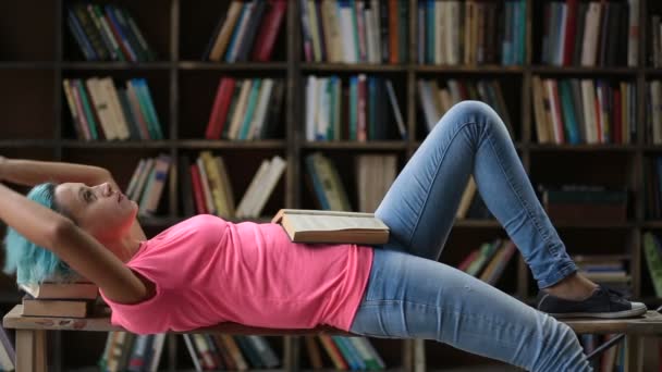 Nadenkend vrouwelijke hipster lezen van een boek in de bibliotheek - Video