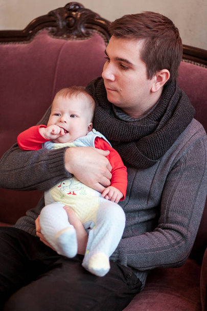 Grrey ニット セーターで父は、ヴィンテージ アームチェアの幼い息子を保持しています。 - 写真・画像
