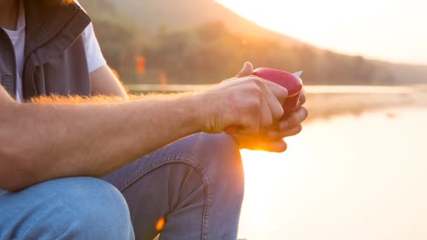 Um homem come uma maçã sentada na margem de um reservatório ao pôr do sol.
 - Filmagem, Vídeo