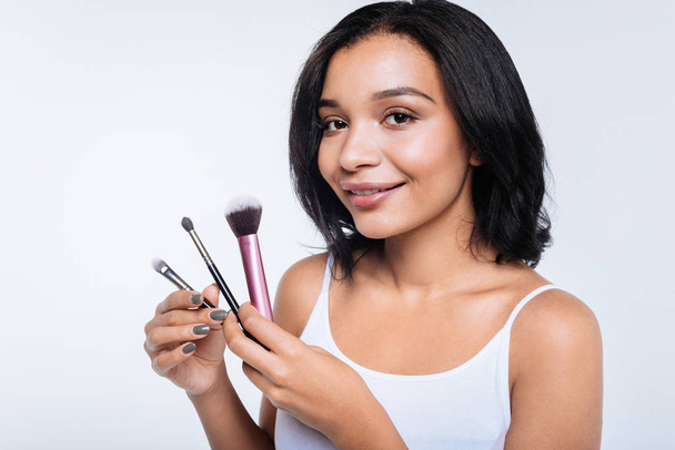 Dark-haired young woman holding makeup brushes - Фото, изображение