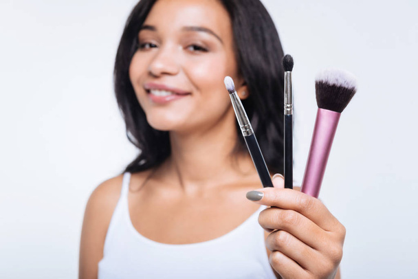 Smiling young woman showing three makeup brushes - Foto, Imagem