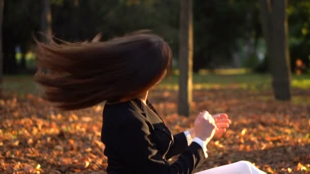 Krásná bruneta dívka sedící na vrh žluté listy - Záběry, video