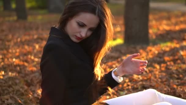 Krásná bruneta dívka sedící na vrh žluté listy - Záběry, video