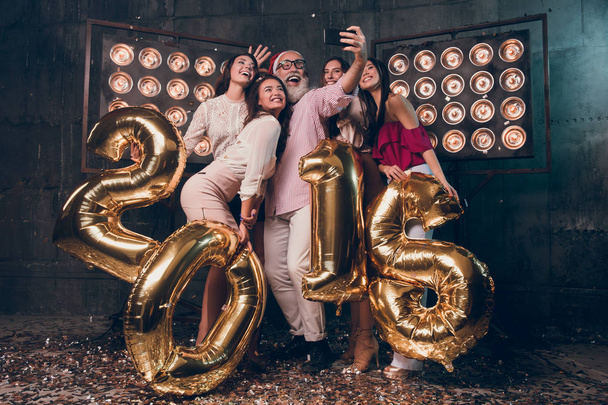 Happy Christmas moments with friends. Group of attractive girls with bearded man in pink shirt and Santa's hat doing selfie and have a fun with gold colored numbers of 2018 New Year. - Photo, Image