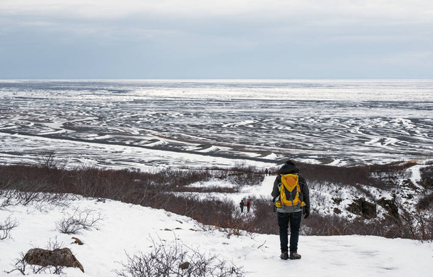 アイスランドで冬には、雪の山の上を歩いて黄色のバックパックを持つ男 - 写真・画像