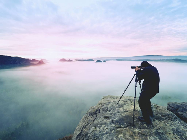 Professional on cliff. Nature photographer takes photos with mirror camera on peak of rock. Dreamy fog - Photo, Image