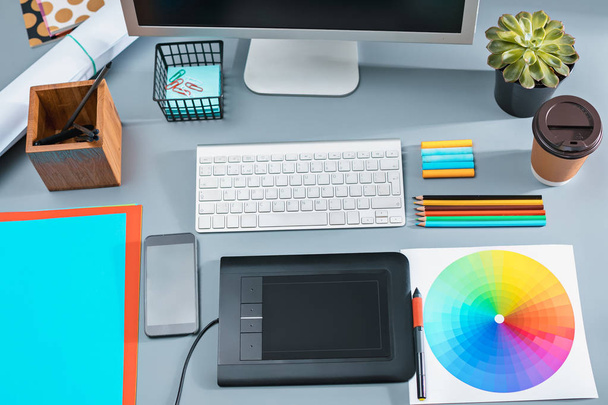 El escritorio gris con portátil, bloc de notas con hoja en blanco, maceta de flores, lápiz y tableta para retocar
 - Foto, Imagen