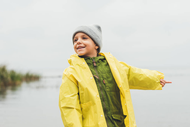 Junge im Regenmantel zeigt aufs Meer - Foto, Bild