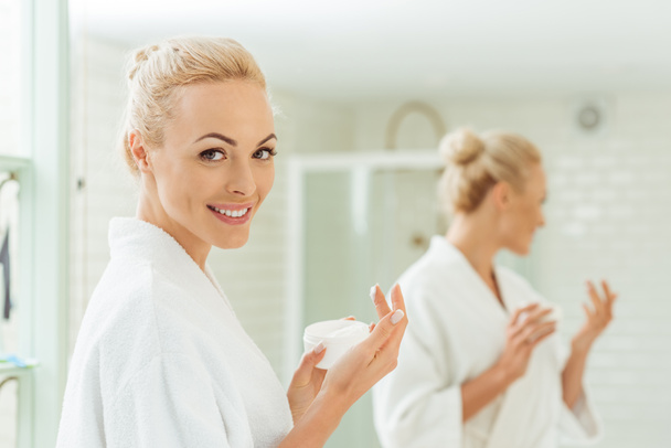 Nainen kylpytakissa soveltamalla kasvovoidetta
 - Valokuva, kuva