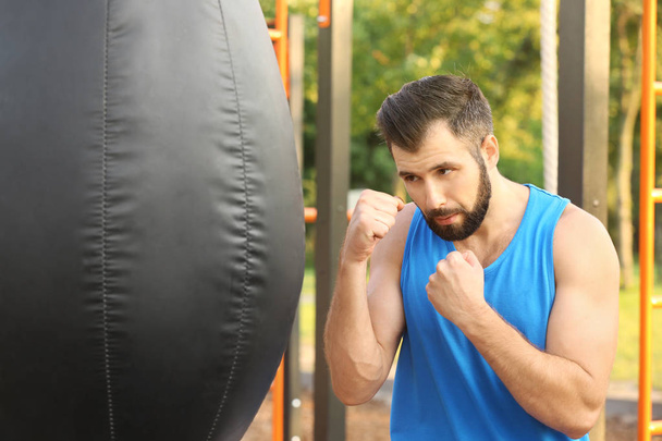 Handsome young man exercising with punching bag in park - Foto, imagen