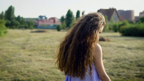 Обратный вид женщины с длинными волосами, позирующей на фоне сельской местности, смотрящей в сторону солнечного света
. - Кадры, видео