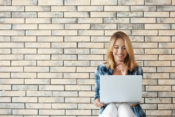 Pretty woman with modern laptop sitting near brick wall - Foto, Imagen