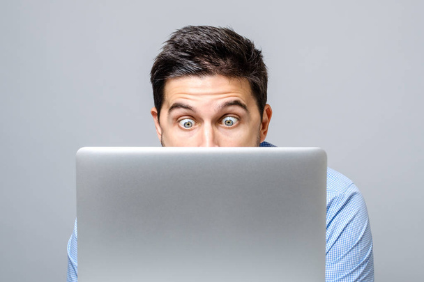 Young shocked man in blue shirt using laptop - Fotó, kép