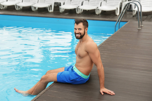 Handsome young man relaxing near blue swimming pool - Fotó, kép