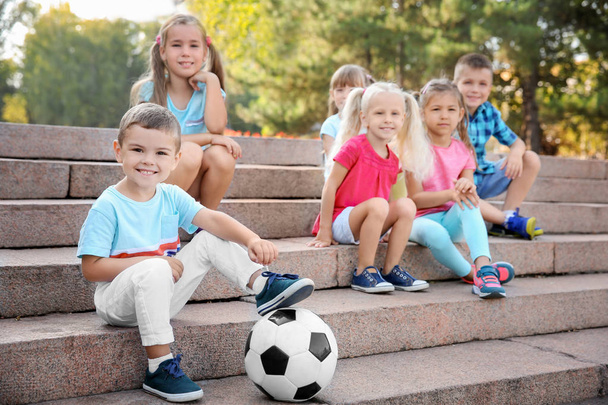 Cute little children with ball sitting on stairs in city park - Фото, изображение