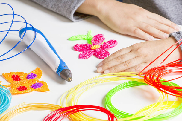 Mains d'enfant et stylo d'impression 3D, filaments colorés sur bureau blanc
. - Photo, image