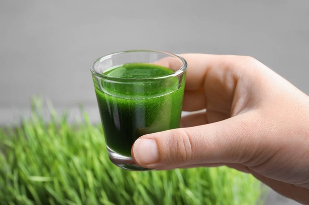 Hand of young man with shot of wheat grass juice - Фото, изображение