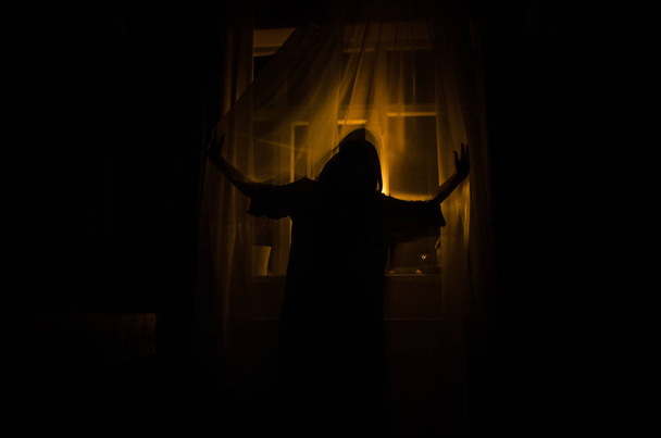 Kauhu nainen ikkunassa puu käsi pidä häkki pelottava kohtaus halloween käsite Hämärtynyt siluetti noita. Valikoiva painopiste
 - Valokuva, kuva