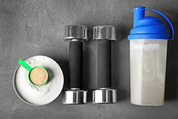 Bottle with protein shake, powder and dumbbells on table - 写真・画像