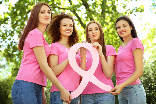 Молоді жінки в рожевих футболках тримають стрічку поінформованості про рак молочної залози на відкритому повітрі
 - Фото, зображення