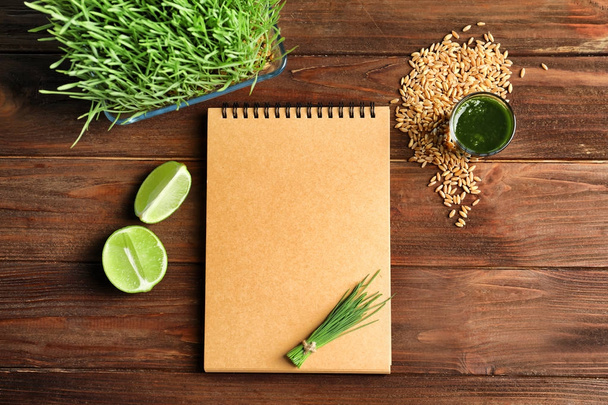 Composition with notebook and shot of healthy wheat grass juice on wooden table - Foto, Imagen