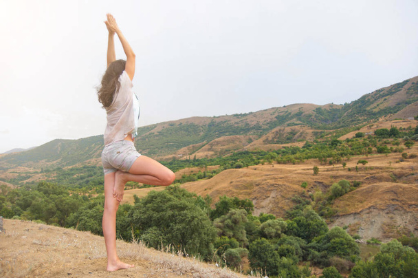 Attractive young female is practicing yoga on the top of the high mountain in the evening - Photo, Image