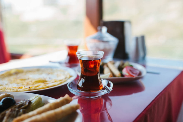 A cup of hot fragrant black tea. Two plates with vegetarian food - fresh vegetables and cheese, cake and drink in glass on red table - Photo, Image