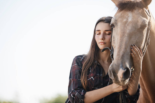 Portrait of a young girl interacting with a horse with closed eyes trying to calm the animal. - Фото, изображение