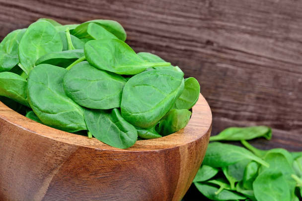 Fresh green baby spinach leaves in a bowl on wooden background - Photo, Image