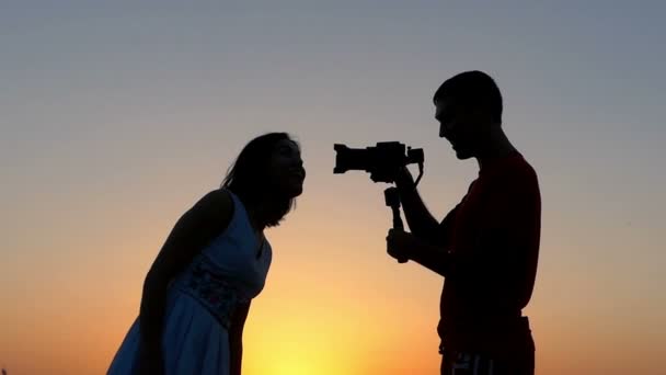 Mladý muž střílí smějící se ženu svým fotoaparátem při západu slunce - Záběry, video