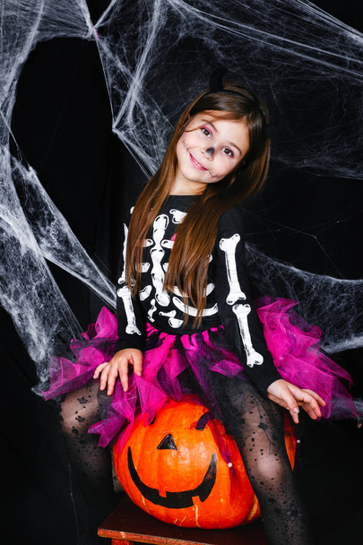 Cute little girl sitting on the pumpkin on black background - 写真・画像