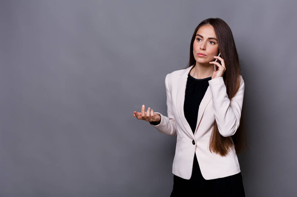 Young businesswoman has call. Studio shot on grey background - Φωτογραφία, εικόνα