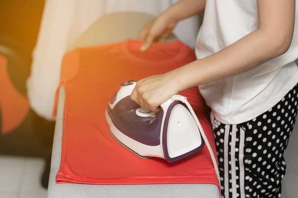 Young woman is using steam iron on her cloths - Foto, immagini