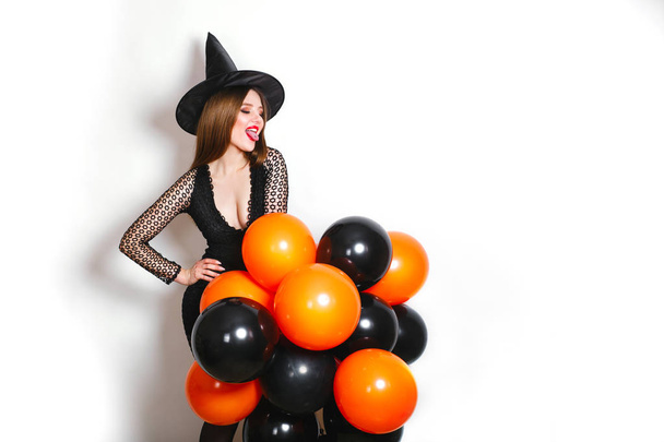 happy sexy women in black witch halloween costumes with orange and black balloon on party over white background - Fotografie, Obrázek
