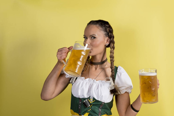 Meisje in Dirndl drinken bier uit de mok op gele achtergrond - Foto, afbeelding