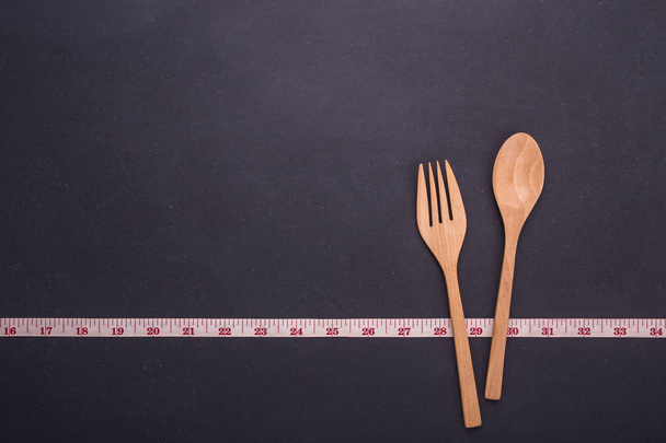 Measurement tape with wooden spoon and fork on black stone board - Foto, immagini