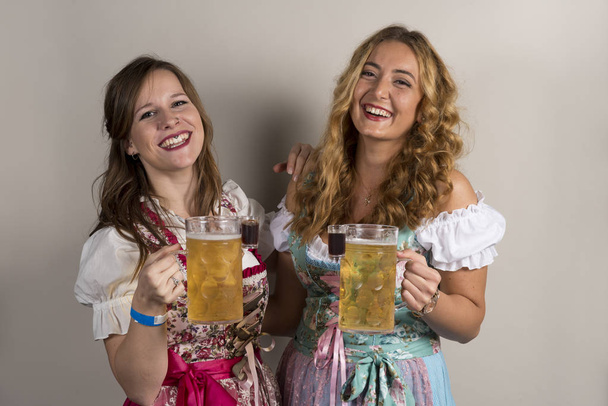 Twee gelukkige dames dragen Dirndls met bier en schoten - Foto, afbeelding