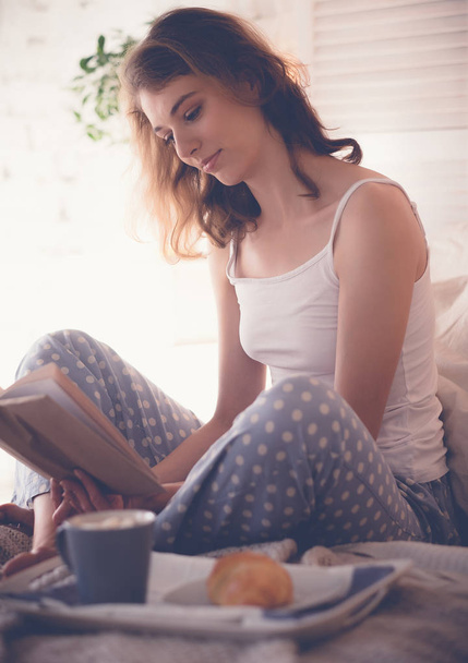 Chica en la cama leyendo y bebiendo café
 - Foto, imagen