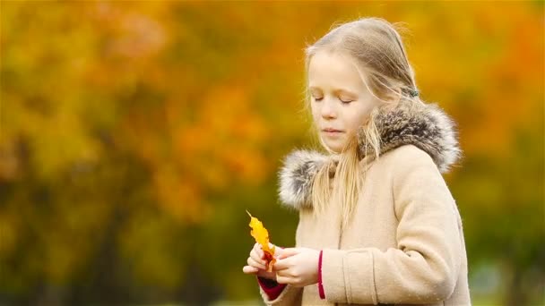 Retrato de adorable niña al aire libre en hermoso día cálido con hoja amarilla en otoño - Metraje, vídeo