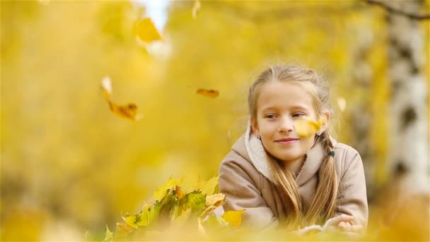 Portrait of adorable little girl with yellow leaves bouquet in fall. Beautiful smiling kid lying on leaves carpet - Footage, Video