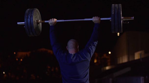 Weightlifter lifts the bar above his head. Strength training with a huge weight. strong crossfit athlete in the middle a heavy snatch lift in a cross-fit box gym - Photo, Image