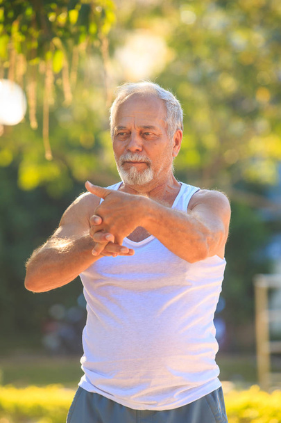 Grey Bearded Old Man in Vest Stretches Fingers in Park - Foto, Imagen