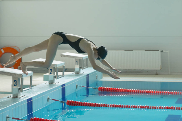 Nuori naisuimari, joka hyppää ja sukeltaa sisäuima-altaaseen.
. - Valokuva, kuva