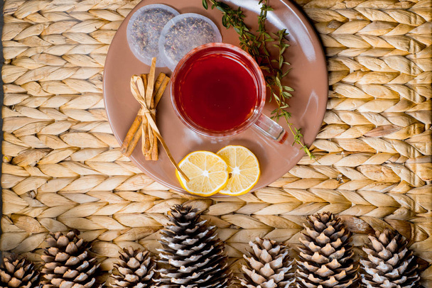 Herbal tea with cinnamon and lemon on a wicker basket. Christmas cones - Фото, зображення