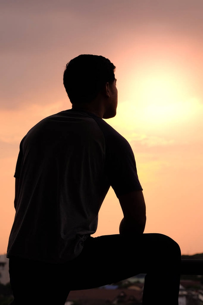 La silhouette di un uomo mette le braccia su una gamba sullo sfondo del tramonto
. - Foto, immagini