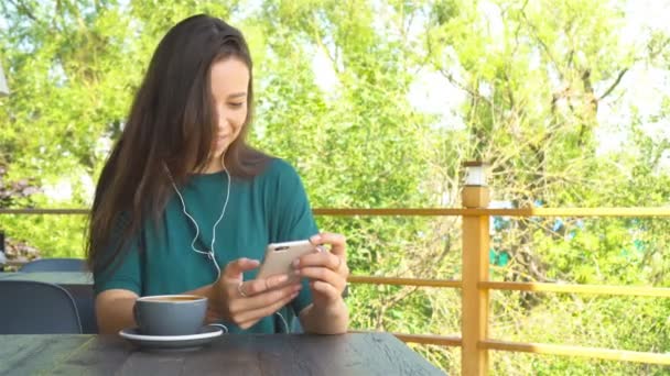 Mujer usando la aplicación en el teléfono inteligente en la cafetería bebiendo café sonriendo y mensajes de texto en el teléfono móvil. Hermosa joven profesional con teléfono móvil
. - Metraje, vídeo