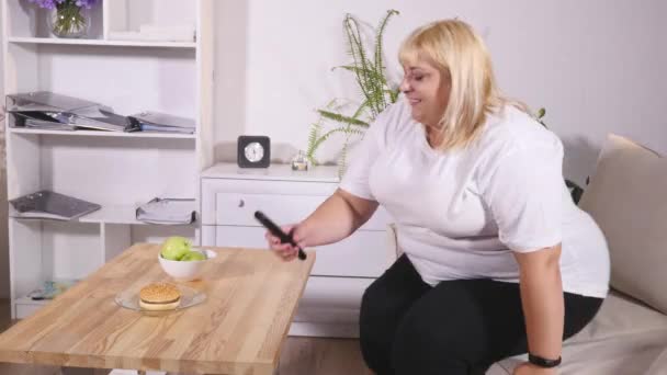 overweight blonde woman sitting on sofa watching TV - Video