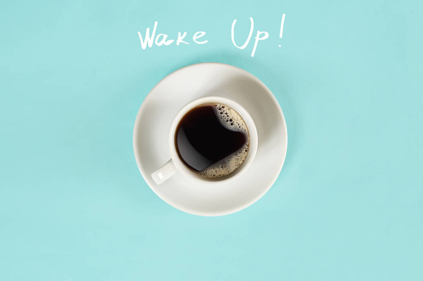 Vista superior de la taza de café negro y letras Wake Up aisladas sobre fondo azul
 - Foto, Imagen