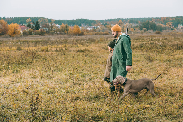Padre e figlio che camminano sul campo con il cane
 - Foto, immagini